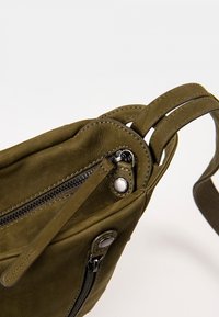 Olivengrüne Ledertasche mit strukturierter Oberfläche, ausgestattet mit einem Reißverschluss, silbernen Hardware-Akzenten und doppelten Stoffgurten.