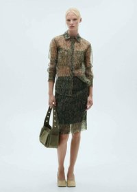 Gennemsigtig slangeprint blouse i grønne nuancer, parret med en matchende pencil nederdel. Tilbehør inkluderer en grøn taske med nitter og beige hæle.