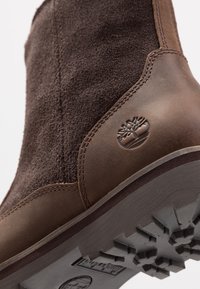 Stivale alla caviglia in suede marrone con dettagli in pelle, punta rotonda e suola in gomma con un motivo a intaglio testurizzato. Logo stampato sul lato.