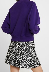 Lila Sweatshirt mit langen Ärmeln und gerippten Bündchen, kombiniert mit einem schwarzen Rock mit einem weißen Leopardenmuster.
