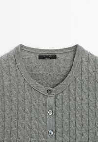 Cardigan gris en maille torsadée avec encolure ronde et trois boutons visibles sur la patte de boutonnage avant.