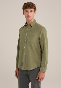 Camicia in corda verde oliva con colletto a punta, tasca frontale e bottoni argentati. Maniche lunghe con polsini abbottonati e finitura texturizzata.