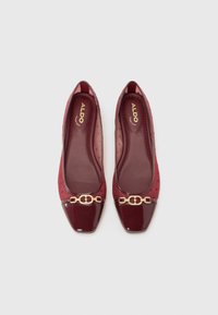 Red patent leather flats with a square toe, featuring a gold chain accent and a dotted sheer panel on the sides. Brand label inside.