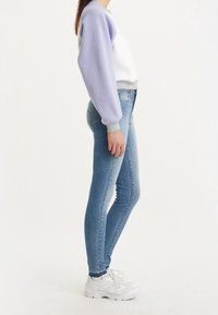 Jeans ajustados azules combinados con una sudadera de bloques de color blanca y morada con puños grises, complementados por zapatillas blancas.