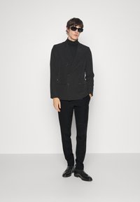 Fekete, dupla soros blazer, hozzá illő garbóval és fazonra szabott nadrággal, kiegészítve fekete napszemüveggel és fényes dress shoes-al.