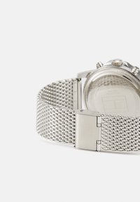 Bracciale in maglia argento con chiusura, caratterizzato da un motivo testurizzato e un quadrante rotondo. Il retro dell'orologio presenta una superficie liscia.