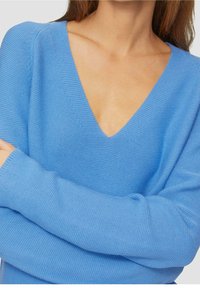 Ljusblå stickad tröja med djup V-ringning, långa ärmar och texturerat tyg. Inga mönster eller detaljer syns.