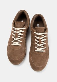 Sneaker in suede marrone con lacci bianchi, punta arrotondata, collo imbottito e dettagli testurizzati. L'interno presenta una fodera in tessuto marrone.