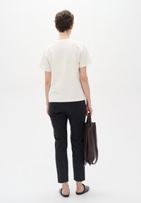 Off-white short-sleeve top paired with black slim-fit pants. A brown leather tote bag is held in one hand. Smooth fabric and simple design.