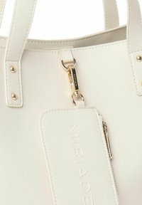 Sac fourre-tout en simili cuir blanc avec une texture lisse, quincaillerie en ton doré, étiquette de marque embossée et poignées robustes.