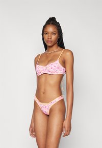 Rozā ziedu bikini komplekts, kurā ietilpst bralete ar plānām siksnām un atbilstošas zemās jostas biksītes ar apmalēm oranžā krāsā.