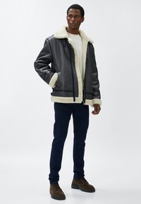 Grå faux læderjakke med kridhvid faux shearling krave og manchetter. Lynlås foran, to sidelommer og mørke denim bukser. Brune snørebåndsstøvler.