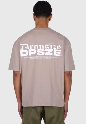 Braunes Baumwoll-T-Shirt mit großen weißen Buchstaben auf dem Rücken, kurzen Ärmeln und einem lockeren Schnitt. Der Saum ist gerade und schlicht.