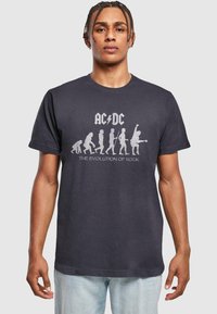 Fekete pamut póló, amelyen az "AC/DC" logó látható, valamint a rock zene fejlődését ábrázoló fehér grafikával.