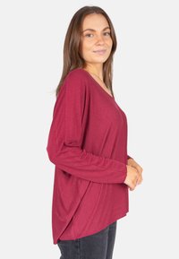 Haut bordeaux à manches longues avec une coupe décontract ée, décolleté en V et texture douce. Stylé avec des épaules légèrement tombantes et des fentes sur les côtés.