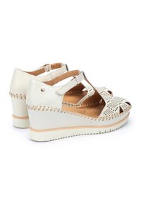 Scarpe con tacco a cuneo in pelle bianca con design perforato e lacci alla caviglia. Presentano dettagli in legno naturale e cuciture lungo i bordi.