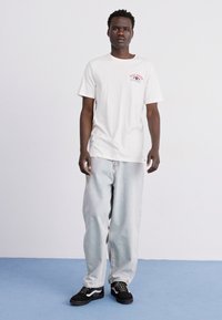 White cotton t-shirt with a colorful graphic on the chest, paired with light blue baggy jeans and black sneakers featuring white accents.