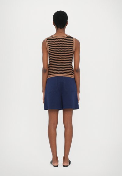 Strick-Tanktop mit schwarz-orangem Zickzackmuster; kombiniert mit marineblauen Shorts, die eine lockere Passform und Gesäßtaschen haben.