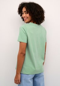 Lichtgroene katoenen t-shirt met korte mouwen en een ronde hals. Gladde textuur, minimaal ontwerp en een losse pasvorm.
