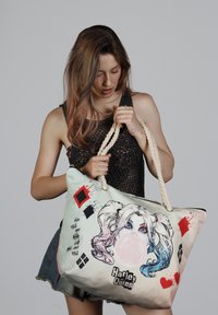 Bolso de lona con asas de cuerda, que presenta un gráfico colorido de la cara de un personaje y formas abstractas en rojo y negro.