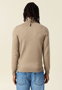 Suéter de cuello alto beige con mangas largas y puños acanalados, combinado con jeans de color azul claro. Textura suave, diseño minimalista, sin patrones.