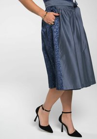 Een knielange rok van donkerblauwe satijn met een panel met bloemenpatroon. Beschikt over zakken en een gladde textuur, gecombineerd met zwarte hoge hakken.