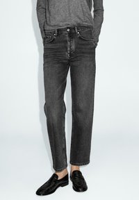 Jeans in denim nero con una vestibilità dritta, dotati di chiusura con bottoni, design a cinque tasche e dettagli di cucitura sottili. Indossati con mocassini neri.
