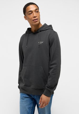 Grau Baumwollhoodie mit einer Fronttasche, Kordelzugkapuze und kleinem Logo auf der Brust. Kombiniert mit blauen Jeans. Glatte Textur.