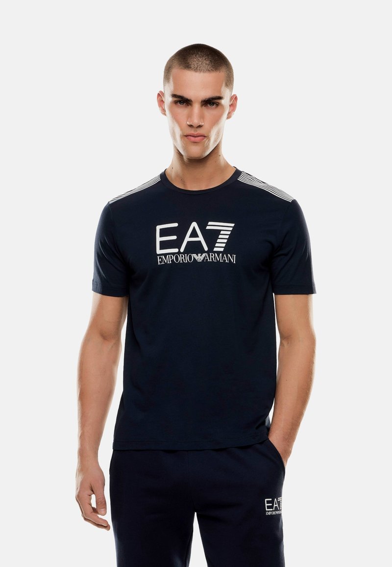 Mörkblå bomullströja med en vit EA7-logotyp, randiga detaljer på axlarna och en klassisk rundhalsdesign.