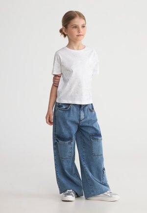 T-shirt bianco a maniche corte con una leggera trama abbinato a pantaloni cargo in denim blu, larghi e con ampie tasche, dal fit rilassato.