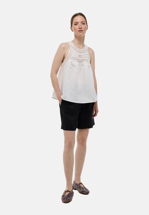 Haut sans manches blanc avec des détails en dentelle intriqués au niveau du col, associé à un short noir et des chaussures à enfiler à motifs.