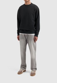 Zwarte sweatshirt met ribgebreide manchetten en zoom, gecombineerd met lichtgrijze jeans en bruine schoenen met witte accenten en veters.
