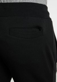 Schwarze Jogginghosen aus glattem Stoff mit elastischem Bund und einer eleganten, versteckten Gesäßtasche für ein minimalistisches Design.