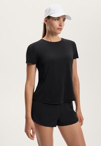 Completo t-shirt a maniche corte nera e pantaloni corti, realizzato in tessuto leggero, abbinato a un cappellino bianco. Tessuto morbido con vestibilità rilassata.
