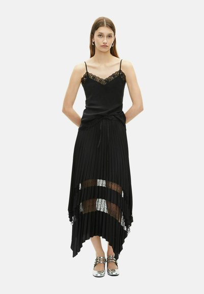 Mujer vistiendo un camisón negro con encaje, una falda negra plisada con paneles horizontales transparentes y zapatos Mary Jane plateados.