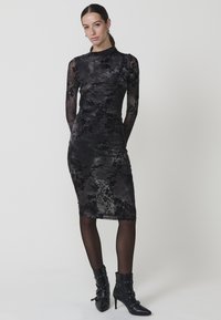 Rochie midi din dantelă neagră, cu mâneci lungi din tull, model floral, formă ajustată și un ușor luciu. Pur tată cu botine negre.
