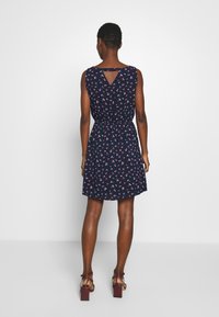 Sukienka w kwiatowy wzór, granatowa, z dopasowaną talią i otworem na plecach. Ma krótkie rękawy i sięga powyżej kolan, zestawiona z sandałami na szerokim obcasie.