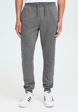 Gray sweatpants made from soft fabric, featuring an elastic waistband with drawstring, tapered legs, and ankle cuffs, paired with white sneakers.