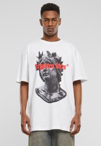 Balta per didelė t-shirt, kurioje pavaizduota juoda ir pilka krūtinės grafika, su raudonu tekstu "pamirstos veido". Trumpomis rankovėmis, laisvas siluetas.