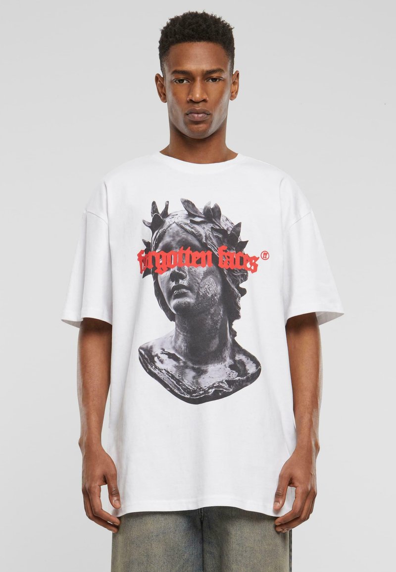 Balta per didelė t-shirt, kurioje pavaizduota juoda ir pilka krūtinės grafika, su raudonu tekstu "pamirstos veido". Trumpomis rankovėmis, laisvas siluetas.