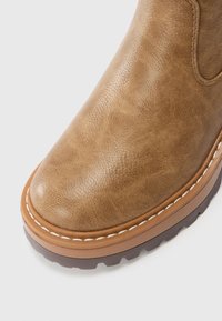 Braune Lederstiefelette mit rundem Zeh, dekorativer weißer Naht und strukturiertem Obermaterial sowie einer robusten braunen Sohle.