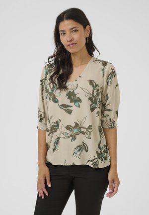 Beige blouse with green floral pattern, V-neck, and gathered short sleeves. Lightweight fabric with a soft texture. Paired with black pants.