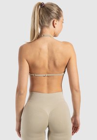 Bralette beige à fermeture au dos avec des fines bretelles, associé à un legging à taille haute en maille côtelée d'une couleur similaire, mettant en avant une texture lisse.