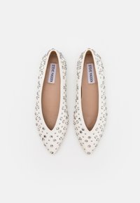 Ballerines blanches à bout pointu ornées de plusieurs strass transparents, présentant une surface lisse ressemblant au cuir et des semelles intérieures beiges avec des étiquettes de marque.