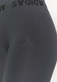 Szare legginsy sportowe o teksturowanym wykończeniu, z szerokim czarnym pasem w talii, na którym znajduje się nadruk "ADIDAS" oraz subtelne logo na udzie.