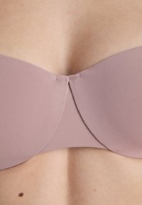 Mauve strapless bh med en glatt tekstur, med en kurvet design, sydd detaljer i midten, og en sømløs finish.