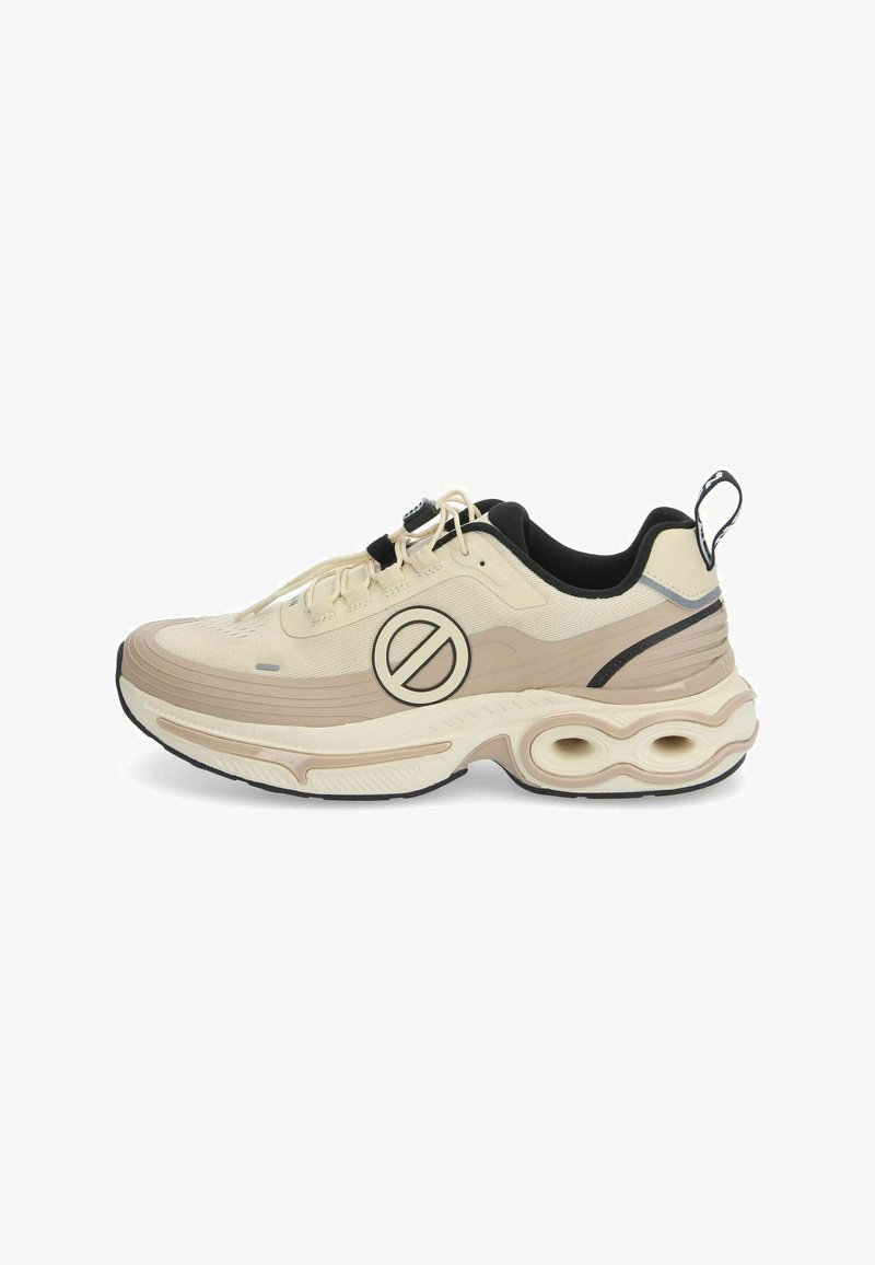 Beige Sport Schuh mit einer strukturierten Oberfläche, schwarzen Akzenten, einem auffälligen runden Logo und einer dicken, gepolsterten Sohle mit hohlen Abschnitten.