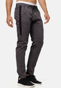 Pantalones de algodón grises con franjas laterales negras, diseño entallado, cintura elástica y puños. Presentan costuras visibles y bolsillos.