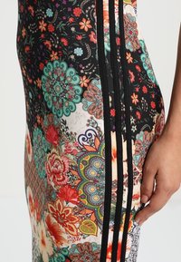 Wielokolorowa sukienka z kwiatowymi i geometrycznymi wzorami, z czarnymi bocznymi paskami, wykonana z elastycznej tkaniny o dopasowanym kroju.