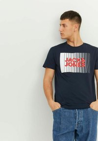 Tricou bleu marin din bumbac cu imprimeu grafic ce prezintă "JACK & JONES" în roșu, pe un fundal dreptunghiular cu linii albe.